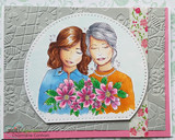 Grey embossed card with a pink base, the two women colored in blue and orange behind a bright pink bouquet on a stitched circle.