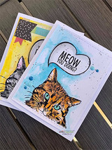 Blue-and-gold card with the tabby on a splattered watercolor panel, 'Meow you doing?' thought bubble above.