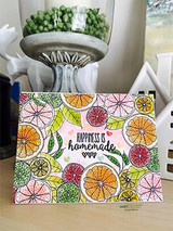 Card standing beside a white house shape, the citrus background colored in soft pinks, corals and greens, with a hand lettered greeting in the center.