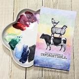 Rainbow watercolor card with the stack and the 'unforgettable' birthday sentiment beside a paint palette.
