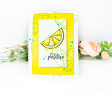 Yellow card with a stitched white panel and one orange slice with leaves, sentiment 'Think positive', photographed with pale blooms.