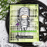 Lime plaid card with green gems on an iron trivet: the mummy above a black “HAPPY HALLOWEEN” banner.