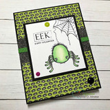 A cuddly green spider dangling from a cobweb on a green Halloween-print card — 'EEK. HAPPY HALLOWEEN.'
