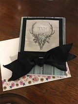 Card with the antler skull and 'HOWDY' stamped in grey on a matted panel with a big black satin bow over teal wood grain paper