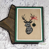 Card with the lettered stag head stamped in black on kraft, with a hanging ornament and red bow on its antler, framed in white and green glitter.