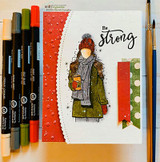 Angie Blom's AngieGirl bundled in a scarf and hat holding a hot drink with 'Happiness, pure and simple,' a red rubber winter stamp on a card.