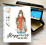 Angie Blom's AngieGirl bundled in a scarf and hat holding a hot drink with 'Happiness, pure and simple,' a red rubber winter stamp on a card.