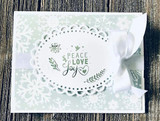 Soft mint snowflake card with a white lace oval and a white ribbon, stamped 'PEACE LOVE joy' with a small sprig and heart.