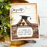 Card using the distressed wood-paneling background behind a graduation basset hound, stamped 'Congrats - it turns out you're smarter than you look.'