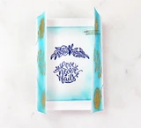 Opened gatefold card showing gold wildflower stems on blue watercolor edges and a navy floral wreath reading 'Love never fails'