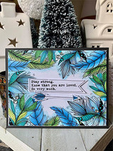 Card with the feather border hand colored in blues and greens over a soft sky background, a white banner across the center reading stay strong, know that you are loved.