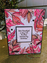 Feather border colored in pinks and corals on a pale lilac panel, tilted on a black card base, with a small framed sentiment about kindness at the center.