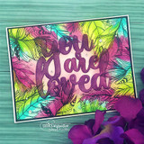 Feather border blended in neon pink, yellow and turquoise, with a large purple glitter die cut reading you are loved laid across the open middle.
