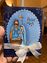 Navy snowflake Peace card of the nativity in an oval frame with a white satin bow.