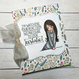 Card with a girl in a grey sweater on a botanical print, 'I'm watching your reaction no pressure to look ecstatic.'