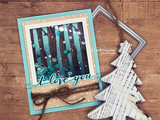 Card with birch trunks coloured teal over a sparkly panel, framed in aqua on a wood background, with 'i love you' on a white banner.
