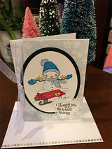 Snowflake print easel card with an oval panel holding the colored snowman on a red sled, sheer ribbon and a heart tag reading Thank you for all the small things.