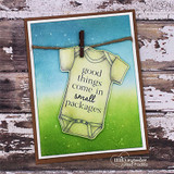 Green onesie pinned to a twine clothesline on a blue and green sky card, stamped 'good things come in small packages'.