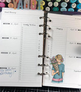 Open ringed planner showing the flower-holding girl tucked onto a dated weekly page.