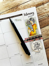 The planner girl and her bouquet decorating a February 2020 monthly calendar page beside a black pen.