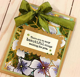 Green card with a wide olive ribbon bow and white die-cut flowers, holding a kraft label reading 'There are so many beautiful things waiting for you.'