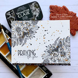 Card with the floral swag stamped in grey and speckled with gold ink, lettered 'PRAYING for you,' shown beside the red rubber stamp and a black ink pad.