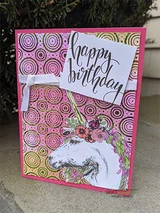 Pink card with a swirl-print background, the unicorn coloured in grey with a bright flower crown, script sentiment 'happy birthday' on a white panel.
