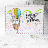 White scalloped card with a pink border and green hills, bunnies riding a rainbow-striped hot air balloon among clouds, script sentiment 'happy birthday'.