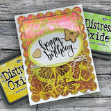 Gold-embossed card with a pink and orange inked panel and a heart window, script sentiment 'happy birthday', styled with distress oxide inks and a wood butterfly.