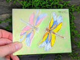 Pastel dragonflies on a green card held in hand.