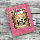 Handmade card with the wooden sign frame inked in warm browns, topped with a pink bloom, stamped 'hang in there' on a pink textured panel.