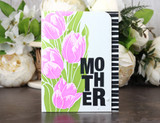 White card with pink stenciled tulips and green leaves beside a black and white striped panel, and the tall stacked MOTHER word block stamped in solid black.
