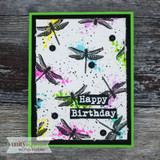 Black framed card with a grey stenciled panel, black dragonflies and bright ink splatters, and a green label with a birthday greeting.