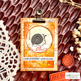 Orange distressed tag card with a snail stamped in a circle, French ephemera marks, a wax seal, and a label with a love is patient greeting.