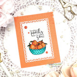 A polka-dot bowl of peaches framed by an orange die-cut border on a white doily background.