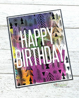 Card with the fir background blended in purple, green and gold behind bold white die-cut 'HAPPY BIRTHDAY' lettering.