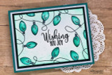 Handmade card featuring the string of vintage Christmas lights framing an A2 card, colored in jewel tones on navy, stamped with 'Wishing you joy'.