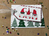 Tag with three red-and-green gnomes over stamped Christmas trees.