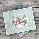 Handmade card with the snow couple colored in soft teal and pink against a snowflake-dotted background, 'Happy Winter.'