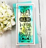 A slimline card with the ornate 'May all be Merry and Bright' panel stamped over a turquoise and yellow blended background, framed in silver and photographed with white hydrangeas.