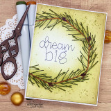 Card with the pine branch stamped in a circle to build an evergreen wreath on a yellow ink blended panel, 'dream big' lettered in the center, styled with a doily and gold ornaments.