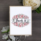 The floral-wreath statement stamp colored in soft pinks on a clean white card among white blooms.