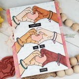 Three pairs of hands in different skin tones forming hearts down a white card with the words together, we do, more, edged in pink plaid.