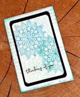 Card with the doily stamped in teal on black inside a frame, 'thinking of you.'