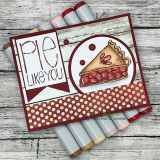 Burgundy card on wood-grain paper with a red 'Pie like you' banner, the cherry pie slice in a circle and a polka dot strip