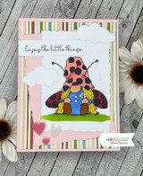 The ladybug gnome colored with a red spotted hat among die-cut clouds on a striped card, reading 'Enjoy the little things.'