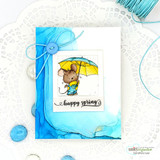 Happy spring card of the mouse with a yellow umbrella on a blue alcohol-ink wash over a doily.