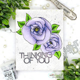 Sample card with two purple blooms and green leaves on a speckled white panel above a bold THINKING OF YOU die cut, styled with pearls and greenery.