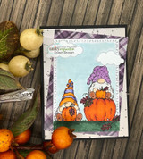 Card with stacked gnomes and pumpkins on plaid background under a blue stamped sky
