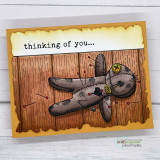 Woodgrain card of a stitched voodoo doll with pins, 'thinking of you…' on torn parchment